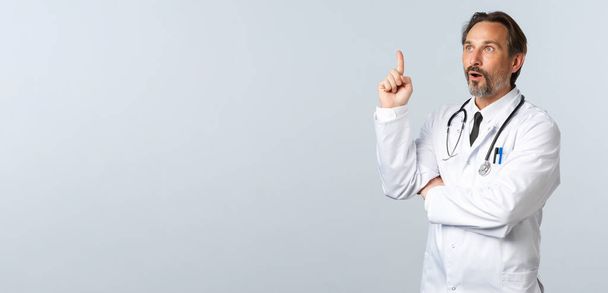 Covid-19, Coronavirus-Ausbruch, Gesundheitspersonal und Pandemiekonzept. Aufgeregte Ärztin im weißen Kittel, erhobener Zeigefinger in Eureka-Geste, ausgezeichnete Idee - Foto, Bild