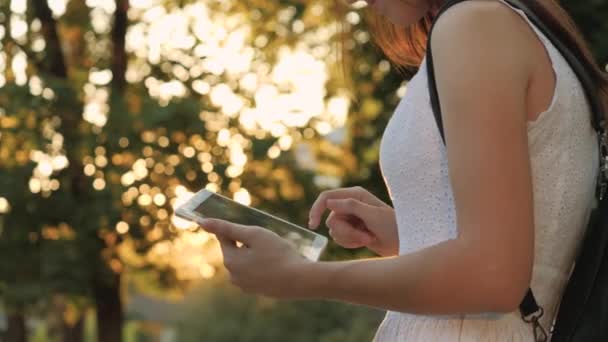 Mladá dívka drží v ruce moderní tablet v záři západu slunce, přejít na internet, paprsky slunce svítí na dotykové obrazovce tabletu, koncept moderních technologií - Záběry, video