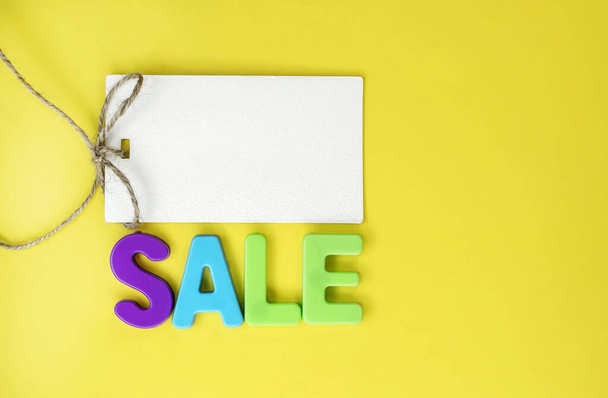On a yellow background, there is a tag for the price tag and the word sale made of colored plastic letters. The concept of discounts and sales. Space for text - Fotoğraf, Görsel