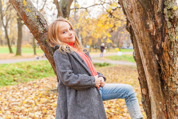 Szczęśliwa młoda dziewczyna uśmiechnięta i siedząca na drzewie w pięknym jesiennym parku na łonie natury spaceruje na świeżym powietrzu. Małe dziecko bawiące się jesienią pomarańczowy żółty tło. Witam koncepcja jesieni - Zdjęcie, obraz