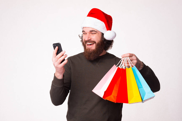 Machen Sie Ihre Einkäufe online über Ihr Telefon. Bärtiger Mann hält Einkaufstüten in der Hand. - Foto, Bild