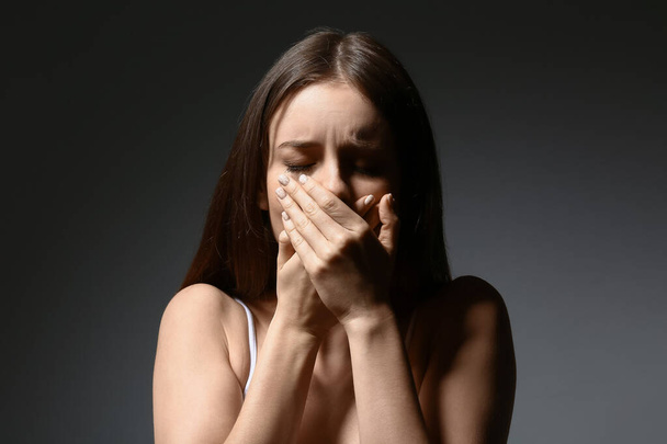 Στρεσαρισμένη νεαρή γυναίκα σε σκούρο φόντο. Έννοια της παρενόχληση - Φωτογραφία, εικόνα