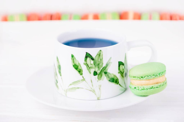 Taza de porcelana de té de flor de guisante de mariposa azul tailandés y macarrón de menta verde o macaron. Copiar espacio - Foto, imagen