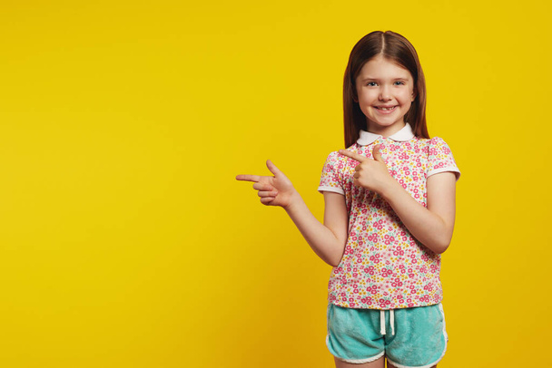 Little cute girl kid, points away with both forefingers, shows blank space - Φωτογραφία, εικόνα