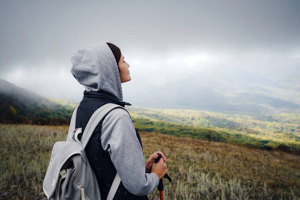 Aziatische reisvrouw staat bij de berg. Koud weer, mist op de heuvels. Herfstwandeling. Het begin van het herfstseizoen. Prachtig mistig weer - Foto, afbeelding
