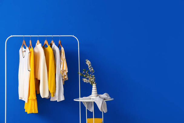 Rack stílusos ruhák és asztal színes háttér - Fotó, kép
