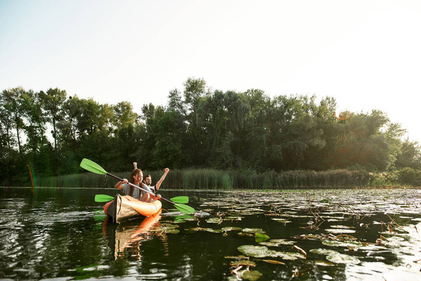 Joyful young mixed couple spending time together, kayaking on river surrounded by wild nature - Zdjęcie, obraz