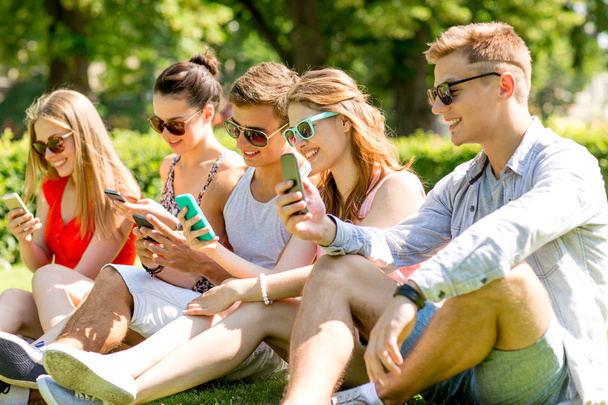 smiling friends with smartphones sitting on grass - Foto, imagen