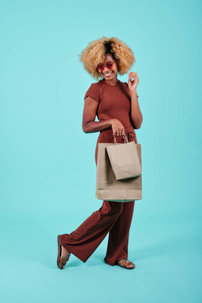 Young afro woman holds paper shopping bags over an isolated background. Black Friday sales season. - Фото, зображення