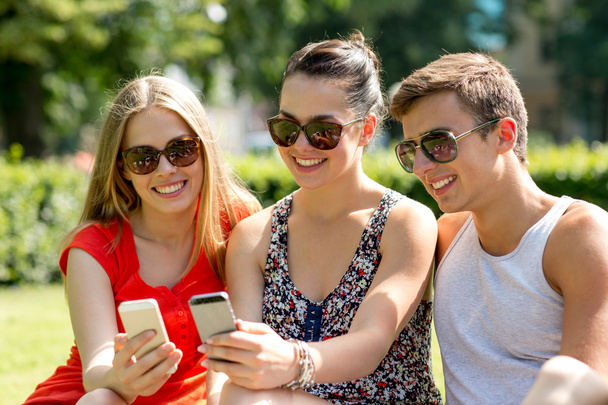 smiling friends with smartphones sitting in park - Foto, imagen