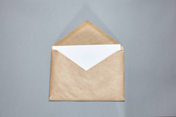 Une enveloppe artisanale marron sur fond gris. Enveloppe artisanale ouverte, branche sur table grise. Une maquette de carte d'invitation. Plat, vue du dessus, espace de copie, mocku - Photo, image