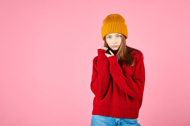 Happy young woman wearing warm sweater and knitted hat on pink background. Smiling hipster with braces having fun. - Fotó, kép