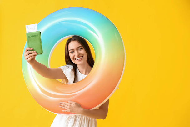 Young woman with passport and inflatable ring on color background - Photo, Image