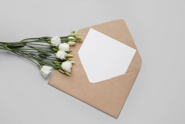 Конверт с пустой карточкой и цветами на светлом фоне - Фото, изображение