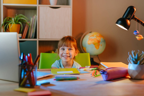 Estudiante de primaria que estudia en línea desde casa usando un portátil sentado en el escritorio de la habitación. Educación a distancia durante el bloqueo pandémico. - Foto, imagen