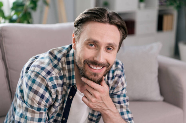 Photo of pretty positive mature guy dressed checkered shirt smiling sitting couch arm chin indoors apartment room - Foto, Imagem