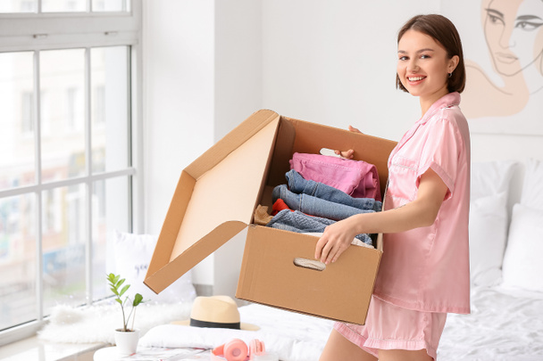 Mujer joven sosteniendo caja de armario con ropa en el dormitorio - Foto, imagen