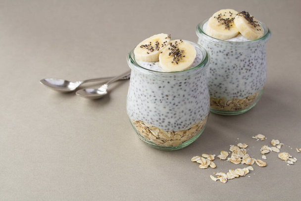 Chia pudding with oat flakes and banana in the glass jars on the gray background - Zdjęcie, obraz