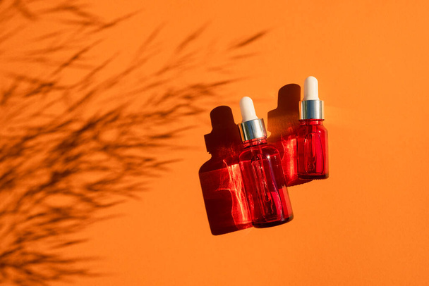 Red glass dropper bottle with silver lid on an orange background. Skincare products with beautiful daylight. - Photo, Image