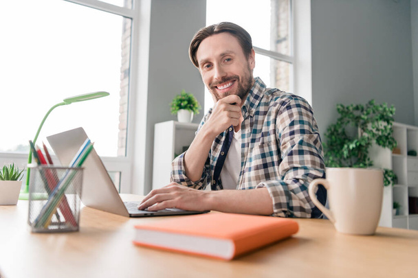 Photo de adorable jeune homme réfléchi porter chemise à carreaux souriant table assise bavarder gadget moderne à l'intérieur bureau maison - Photo, image