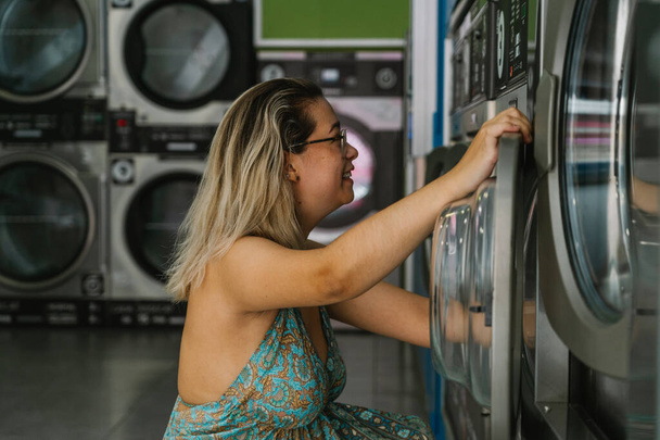 mulher loira usando uma máquina de lavar roupa em uma lavanderia - Foto, Imagem