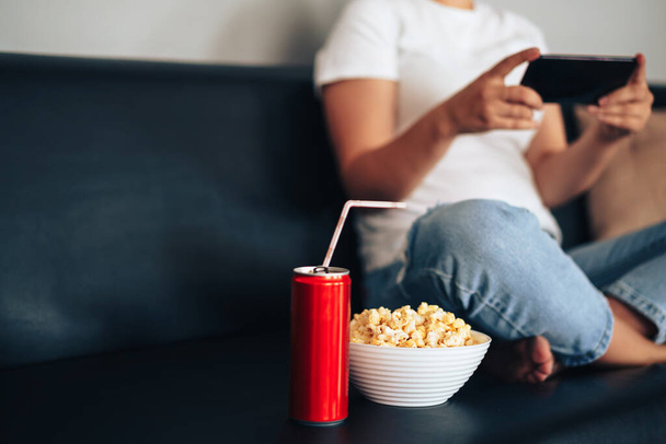 Juice can with straw and cup with popcorn in front of girl holding smartphone. - Foto, immagini