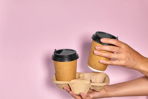 Крупним планом на рожевому тлі, рука жінки тримає паперову чашку з кавою на підставці. Кава або чай, щоб піти. Люди передають один одному чашку кави, доставку кави
. - Фото, зображення
