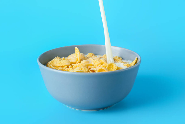 Наливание молока в миску с вкусными кукурузными хлопьями на цветном фоне - Фото, изображение