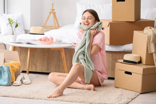 Jonge vrouw met trui en kledingkast dozen in de slaapkamer - Foto, afbeelding