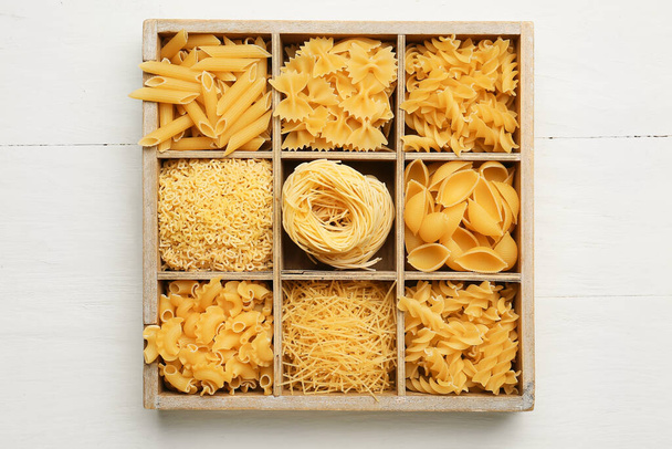 Boîte avec différents types de pâtes non cuites sur fond blanc en bois - Photo, image