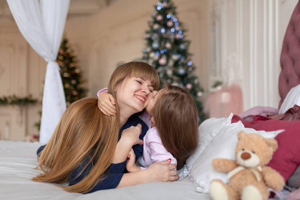 Little girl spends time playing with mom while lying in bed. Christmas tale. Happy childhood. - Zdjęcie, obraz