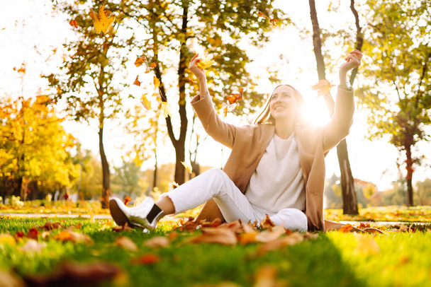 Happy woman having fun and playing with autumn yellow leaves in park. Lifestyle. Relax, nature concept. Autumn style. - Photo, image