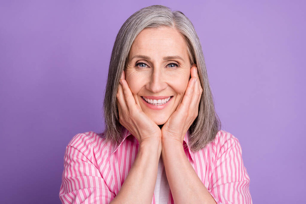 Фото пожилой веселой женщины счастливой позитивной улыбкой руки касаются щек изолированы на фиолетовом фоне цвета - Фото, изображение