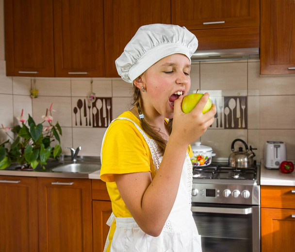ein Mädchen in Kochkleidung hält einen Apfel in der Hand - Foto, Bild
