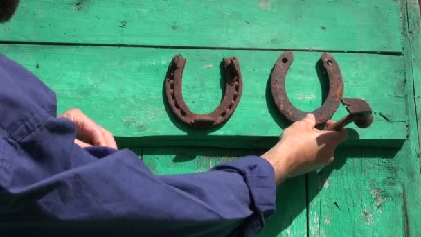 Martillando antiguos símbolos de suerte de herradura oxidada en la puerta de la granja
 - Imágenes, Vídeo