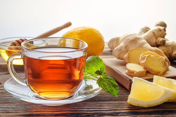 Ginger tea with lemon and mint in glass cup on wooden background. - Foto, afbeelding