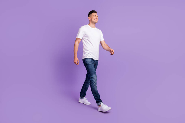 Full body photo of charming positive cheerful man look walk empty space smile isolated on purple color background - Photo, Image
