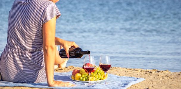 ビーチでワインのグラスを持つ美しい笑顔の女性。フルーツ赤ワイン。選択的焦点. - 写真・画像