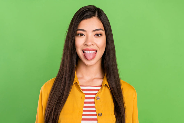 Photo of cute tricky young woman dressed casual clothes showing tongue isolated green color background - Foto, immagini