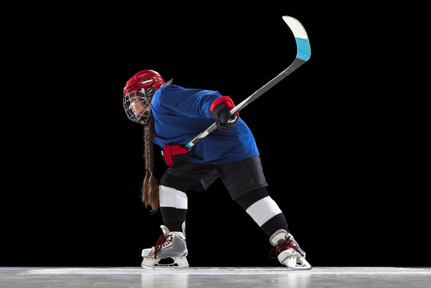 Portrait complet d'une enfant fille, joueuse de hockey isolée sur fond noir. Vue latérale - Photo, image