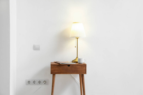 Glowing lamp and magazine on table near light wall - Photo, Image
