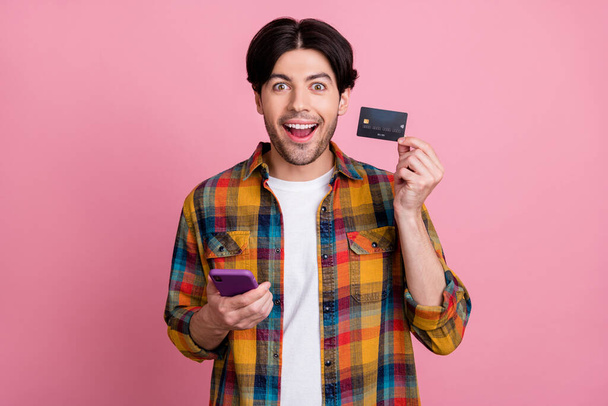 Photo of charming sweet guy dressed checkered clothes typing modern device holding card isolated pink color background - Fotoğraf, Görsel