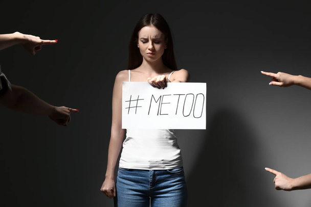 Gente señalando a una joven que sostiene papel con la etiqueta MeToo sobre un fondo oscuro - Foto, Imagen