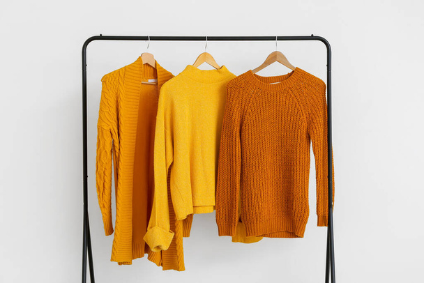 Rack with stylish knitted clothes near light wall - 写真・画像