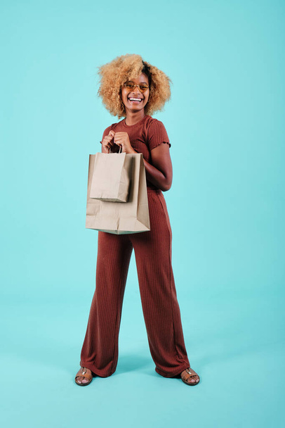 Молодая черная женщина выглядит взволнованной после покупок, держа в руках бумажные пакеты. - Фото, изображение