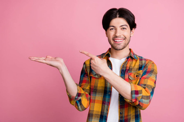 Photo of sweet pretty young gentleman wear plaid outfit holding arm pointing finger empty space smiling isolated pink color background - Photo, Image
