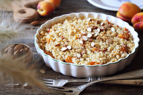 Summer dessert. Fresh apricot crumble, almonds dressing in ceramic dish on wooden background - Photo, Image