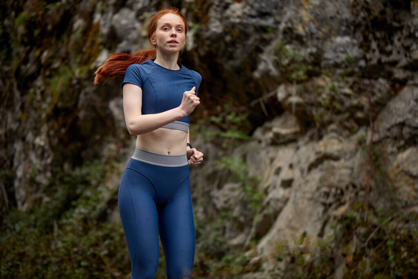 Young slim redhead woman warming up on mountains before workout, running - Фото, изображение