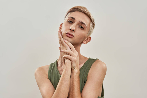 Portrait of sensual androgynous transgender young man with makeup touching his face while posing isolated over light background - Foto, afbeelding