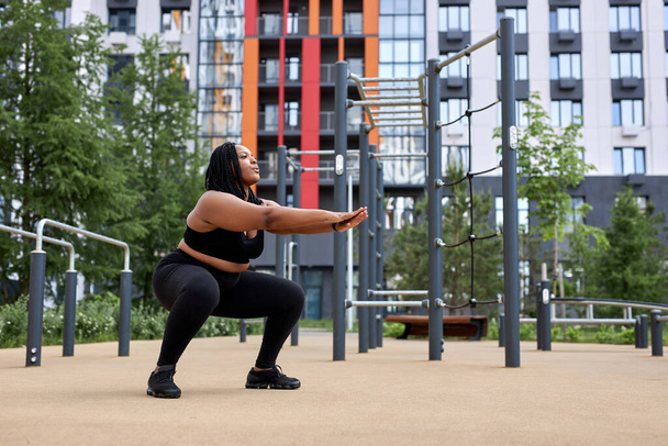 Overweight fat afro american woman squats in sports ground. Weight losing, obesity - Fotografie, Obrázek